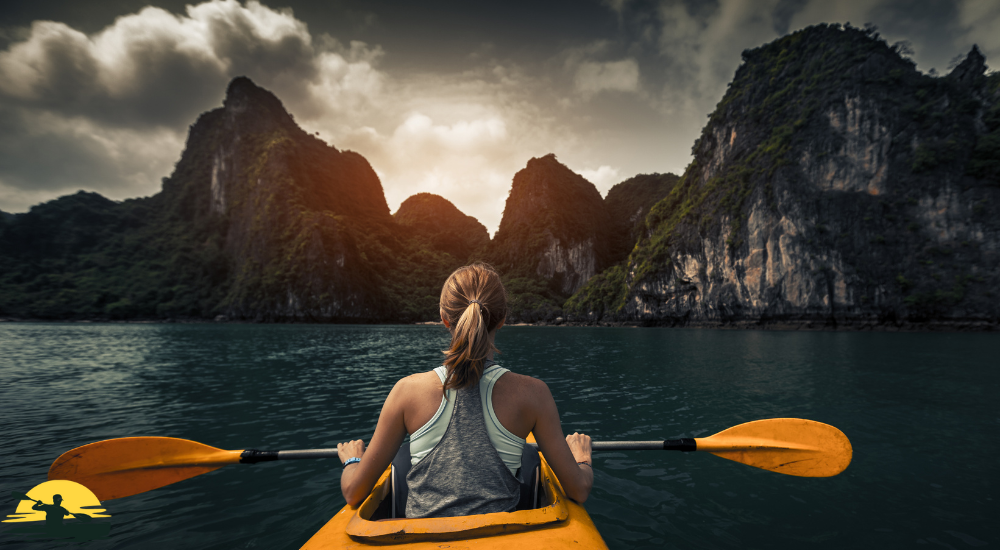 A lady is kayaking in the sea in front of the mountain